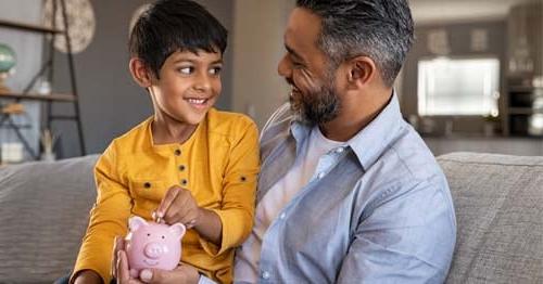 Young student in a yellow shirt is looking at their father holding a pink piggy bank